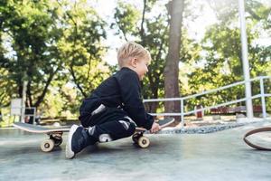 jong kind zittend in de park Aan een skateboard. foto