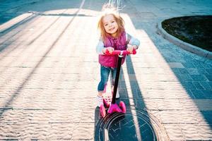 weinig meisje met blond haar- ritten Aan scooter foto