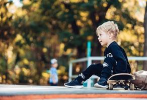 jong kind zittend in de park Aan een skateboard. foto