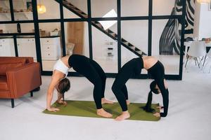 twee jong vrouw praktijken brug houding staand Aan een yoga mat. foto
