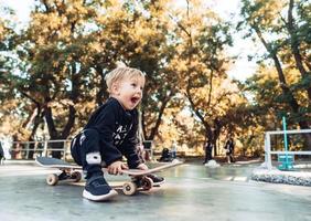 jong kind zittend in de park Aan een skateboard. foto