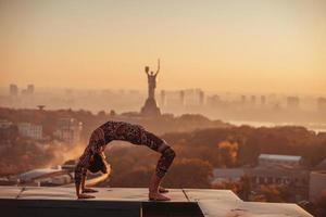 vrouw aan het doen yoga Aan de dak van een wolkenkrabber in groot stad. foto