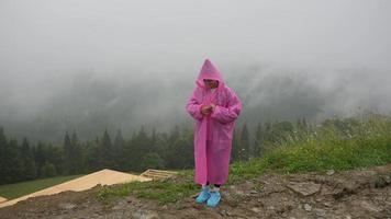 aantrekkelijk wandelaar meisje in een roze regenjas staat Aan een berg foto