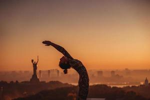 vrouw aan het doen yoga Aan de dak van een wolkenkrabber in groot stad. foto