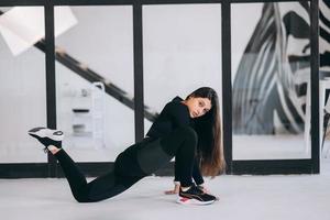 jong vrouw vervelend zwart sport- pak oefenen yoga houding binnenshuis. foto