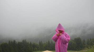 aantrekkelijk wandelaar meisje in een roze regenjas staat Aan een berg foto