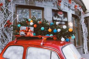 rood retro auto met een Kerstmis boom Spar gebonden naar de dak. foto