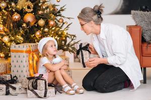 gelukkig grootmoeder geven Kerstmis Cadeau naar opgewonden kleindochter. foto