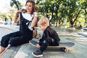 jong moeder geeft les haar weinig jongen naar rijden een skateboard foto