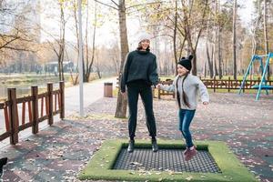 mam en haar dochter jumping samen Aan trampoline in herfst park foto