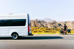 weg kant visie wit busje voorbij gaan aan mannetje fietser Aan kant van weg in Armenië toneel- natuur buitenshuis. fiets toeren buitenshuis en fiets vervoer concept foto