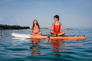 mam en weinig dochter aan het doen yoga Aan de peddelen bord foto