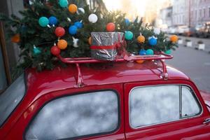 rood retro auto met een Kerstmis boom Spar gebonden naar de dak. foto