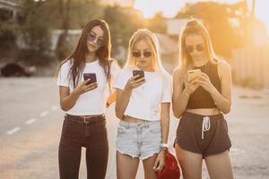 drie aantrekkelijk Dames zijn staand Aan auto parkeren met smartphones foto