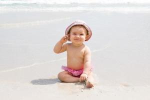 mooi weinig meisje is zittend Bij strand in de buurt naar zee en spelen met zand. foto