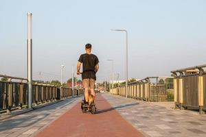 Europese Mens is rijden Aan elektrisch scooter met zijn klein hond. wandelen met hond Aan leeg straat van stad Bij zonnig dag. foto