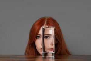 vervormd gezicht van vrouw op zoek door glas van water foto