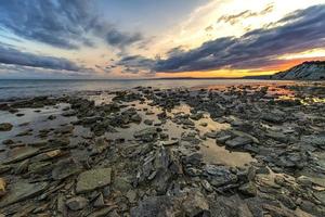 steen strand Bij zonsondergang. schemering zee en lucht. dramatisch lucht en wolken. natuur landschap. foto