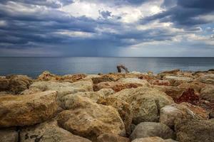 kleurrijk stenen Aan een kust met stormachtig wolken Bij de horizon. horizontaal visie foto