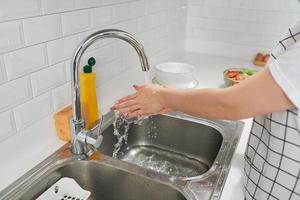 vrouw het wassen handen in wastafel voordat Koken Bij huis keuken. foto