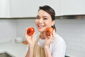 portret van haar ze mooi hoor aantrekkelijk lief zelfverzekerd vrolijk vrolijk meisje Holding in handen tomaat Koken elke dag huiselijk maaltijd lunch lunch veg in modern licht wit interieur keuken foto