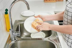 bijgesneden beeld van aantrekkelijk jong vrouw is het wassen gerechten terwijl aan het doen schoonmaak Bij huis foto