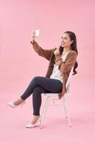 glimlachen jong vrouw maken selfie foto Aan smartphone over- roze achtergrond