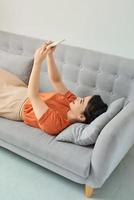 gelukkig vrouw gebruik makend van mobiel telefoon Aan sofa foto