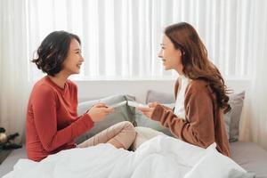 glimlachen twee Aziatisch jong lief paar rust Aan wit bed en gelukkig spelen met smartphone en sociaal media. foto