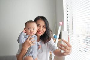 jong moeder is maken selfie met haar aanbiddelijk weinig baby en glimlachen foto