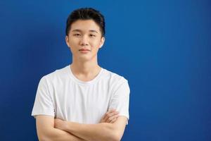 glimlachen knap Mens in t-shirt staand met gekruiste armen geïsoleerd Aan blauw achtergrond foto