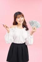 portret van jong Aziatisch vrouw tonen bundel van geld bankbiljetten Aan roze achtergrond foto