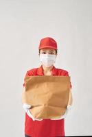 Gezondheid bescherming, veiligheid en pandemisch concept - levering vrouw in beschermend gezicht masker met voedsel in papier zak over- roze achtergrond foto