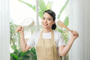 vrouw in schort in hand- frituren pan en keuken spatel in de buurt groot venster foto