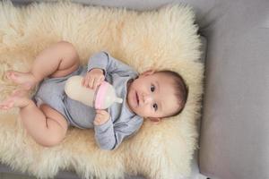 klein schattig meisje drinken melk terwijl aan het liegen Aan blauw sofa Bij huis foto