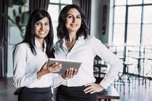 twee vrolijke vrouwelijke collega's met behulp van tablet-computer in café