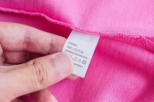 vrouw lezing Aan wasserij zorg het wassen instructies kleren etiket Aan roze katoen overhemd foto