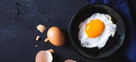 menu Koken in keuken ei gebakken ei in de pan en vers rauw eieren Aan zwart houten achtergrond foto