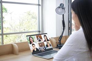 Aziatisch Dames werken van huis ze is hebben een groep video babbelen vergadering met haar collega's Aan haar laptop. foto
