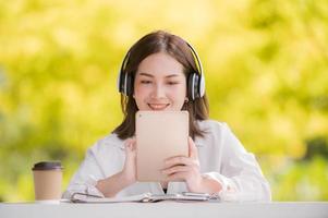 een mooi Aziatisch vrouw ontspannende in de terug tuin met hoofdtelefoons Verbinden via de internet voor online werk en studie foto