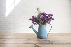 paars droog bloemen in blauw blik gieter bloem pot Aan houten tafel met wit steen muur achtergrond foto