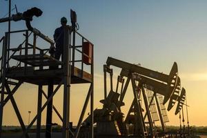 silhouet van olie arbeiders werken in olie tuigage of olie velden en gas- station in de avond met mooi zonsondergang. foto