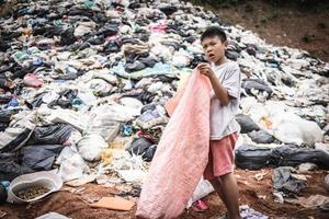 een arm jongen verzamelen vuilnis verspilling van een stortplaats plaats in de buitenwijken. armoede en kind arbeid concept, menselijk mensenhandel. foto