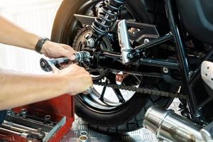 monteur gebruik makend van een moersleutel en stopcontact naar verwijderen en vervangen achterzijde motorfiets wiel, werken in garage onderhoud, reparatie motorfiets concept .selectief focus foto