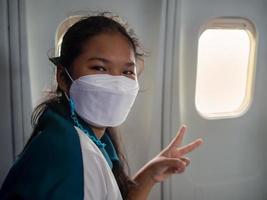 een vrouw vervelend een masker is zittend door de venster van een vliegtuig. foto
