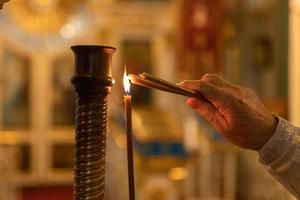 orthodoxe kerk. Christendom. hand van priester die brandende kaarsen aansteekt in de traditionele orthodoxe kerk op paasavond of kerstmis. religie geloof bidden symbool. foto