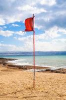 rood vlag Aan strand van dood zee in zonnig winter dag foto