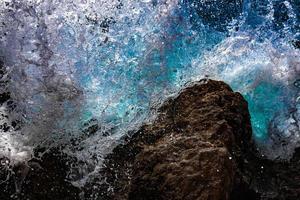 turkoois golven van zee water breken en verstuiven druppels Aan stenen. detailopname. rood zee foto