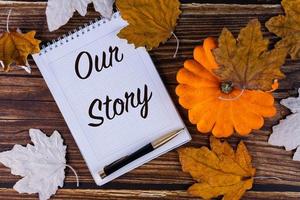 onze verhaal, inscriptie, tekst is geschreven in een wit notitieboekje met een pen Aan een achtergrond van herfst, esdoorn, bladeren en oud planken. foto