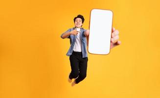 beeld van jumping omhoog Aziatisch Mens Holding smartphone in hand, geïsoleerd Aan geel achtergrond foto